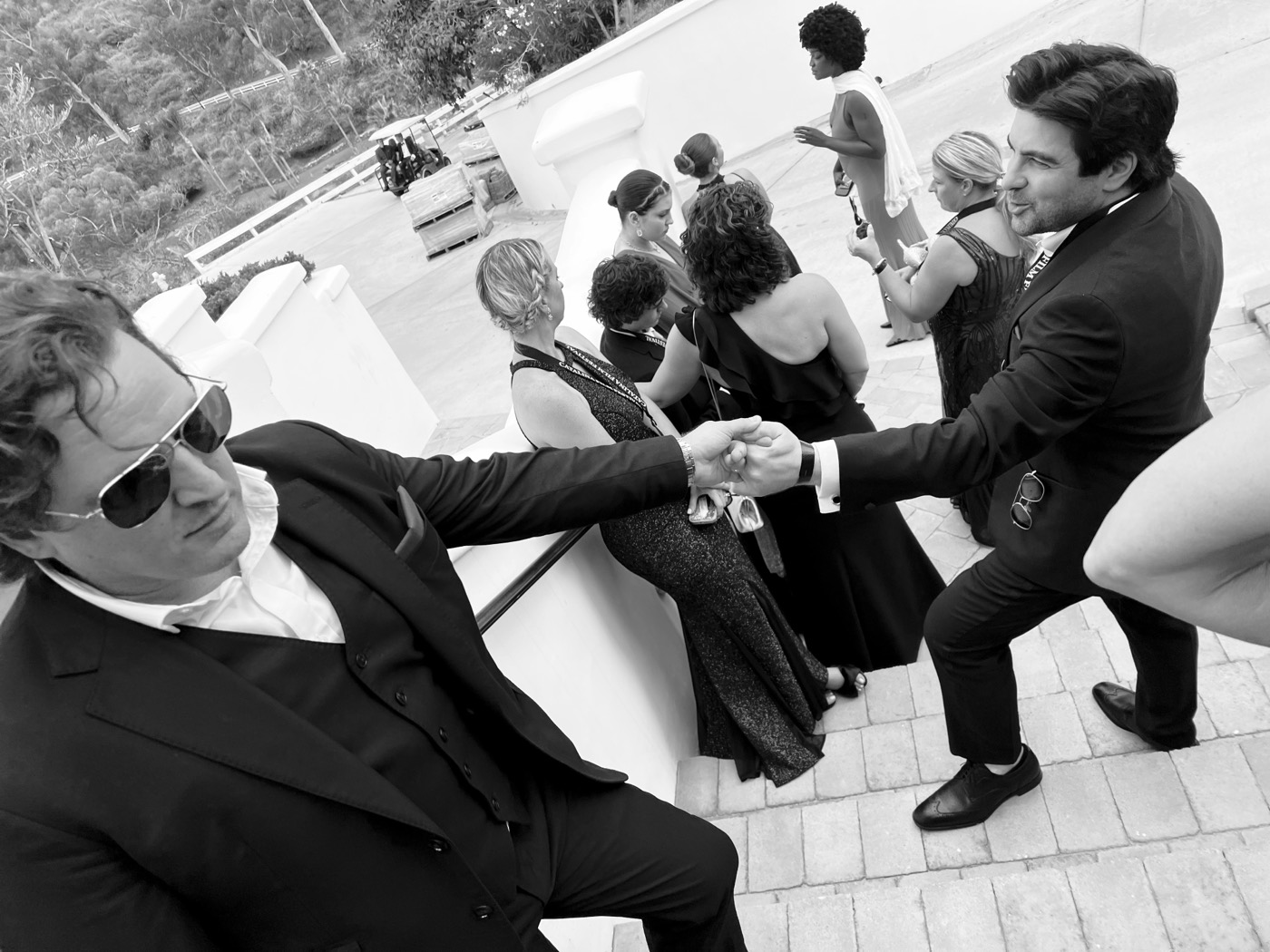 Jason Pelsey, seated in sunglasses, shaking hands with Remi Gangarossa at the festival, black and white