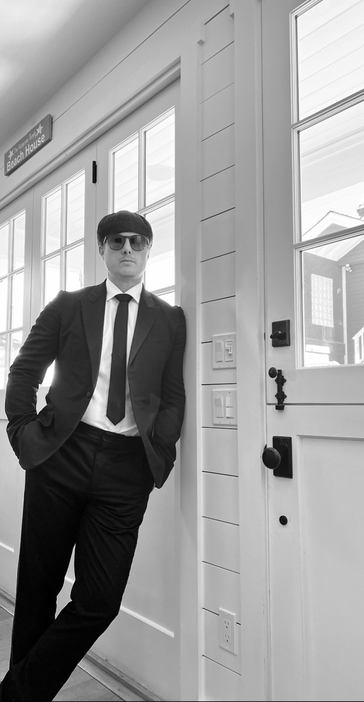 Rob Watt in a suit, tie, cap and sunglasses leaning in a doorway on Catalina Island, black and white