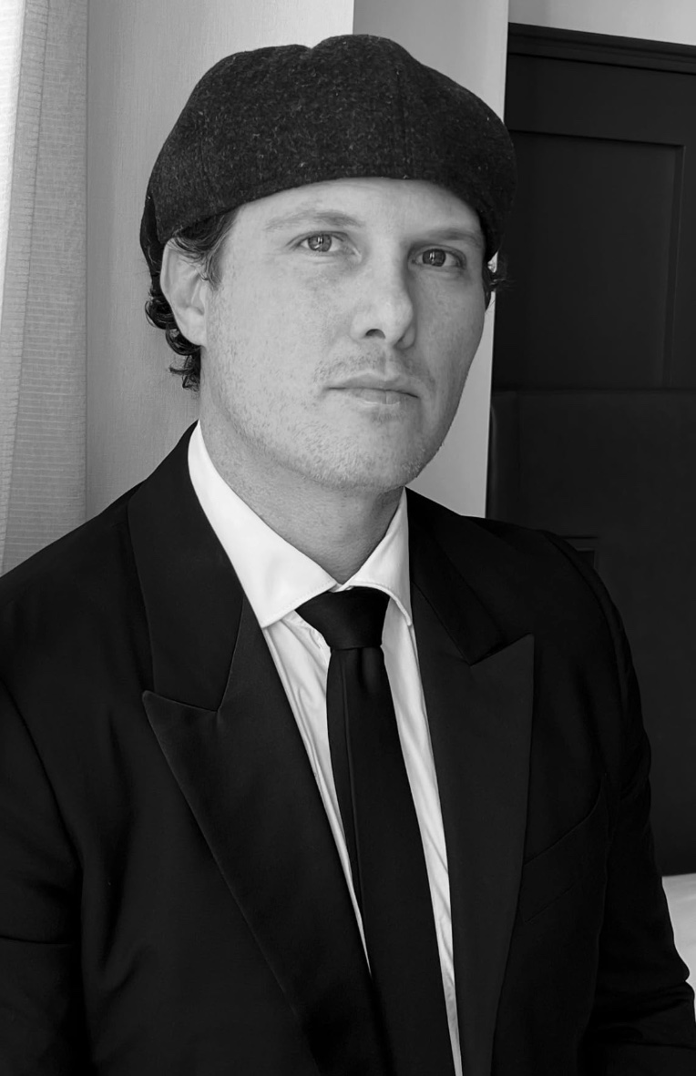Portrait of filmmaker Rob Watt in a suit and flat cap, black and white