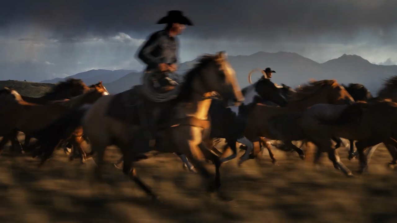 Cowboys driving a herd of galloping horses beneath stormy mountains, from the Boot Barn USA 250 commercial