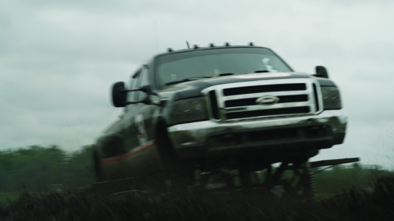 Lifted truck charging over a grassy rise toward the camera under a stormy sky, from the Boot Barn Wheels Off commercial